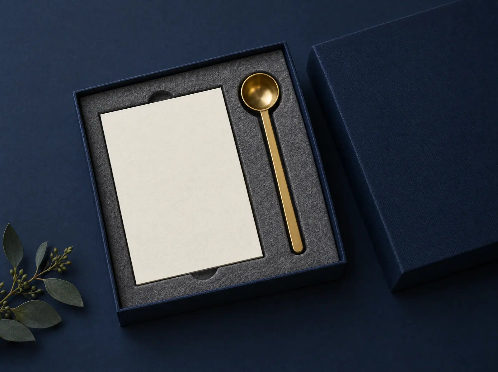 An open navy gift box holding a blank card and a brass measuring scoop